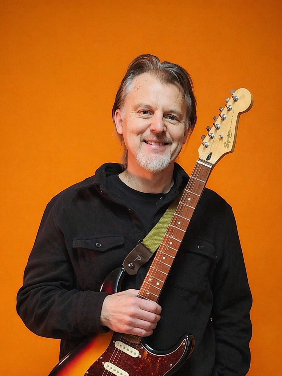 Smiling man holding an electric guitar against an orange background.
