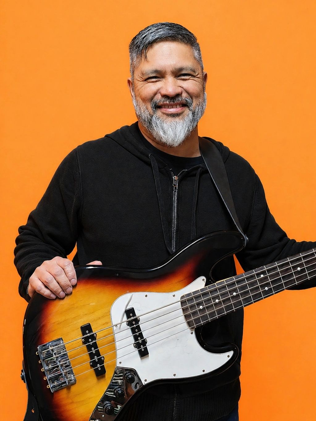 Smiling man holding an electric bass guitar against an orange background.