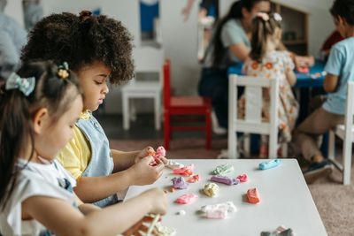 Children playing and molding colorful clay at a table in a classroom.