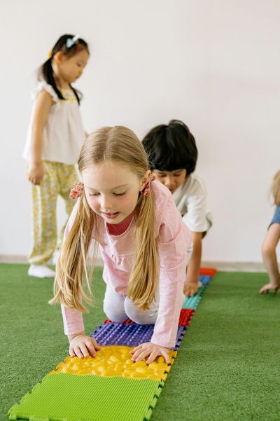 Children playing and crawling on colorful textured mats on a green carpet.