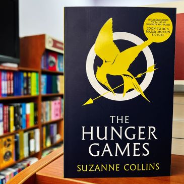 Book cover of The Hunger Games by Suzanne Collins with yellow mockingjay symbol.