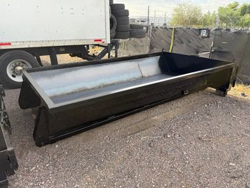 Large black metal container bed outdoors on gravel ground.