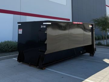 A large black dumpster parked in an empty lot outside a modern building.