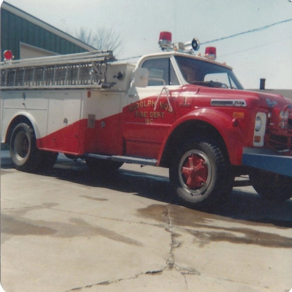 Vintage Rudolph Volunteer Fire Department fire truck parked outside.