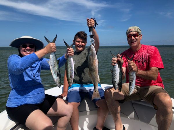 Three people proudly holding their caught fish on a boat.