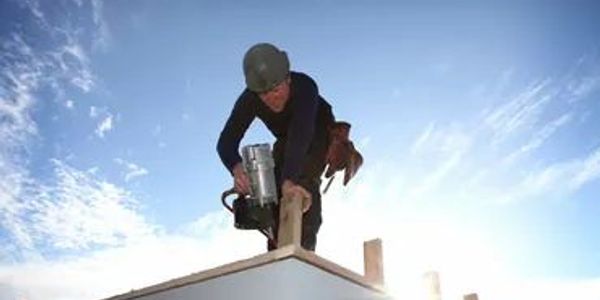 A construction worker using a nail gun on a rooftop under a clear sky.