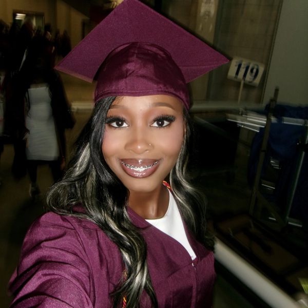 Smiling graduate in maroon cap and gown taking a selfie.