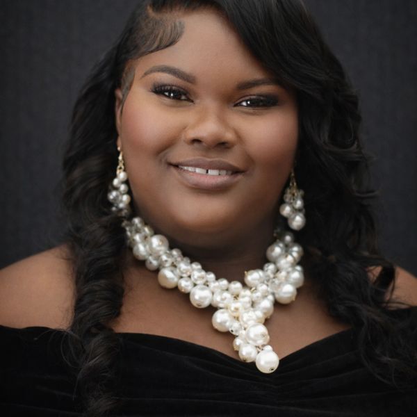 Close-up portrait of a smiling woman with pearl necklace and earrings.