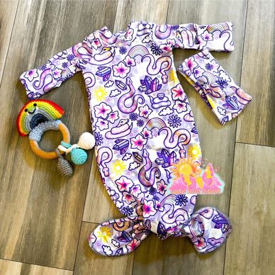 Colorful baby gown with matching hat and rainbow rattle on wooden floor.