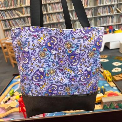 Colorful tote bag with celestial and floral patterns on a purple background.