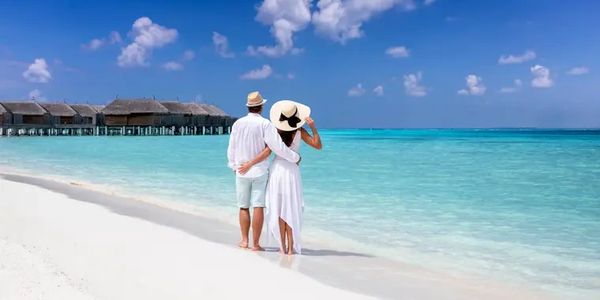 Couple enjoying a serene beach with clear blue water and overwater bungalows.