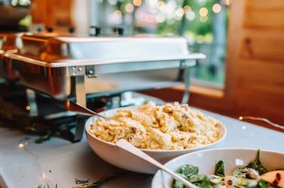 Chafing dishes and white bowls are arranged on a long table for a wedding dinner and reception.