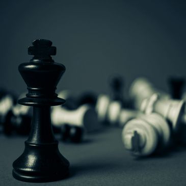 A photo of a black chess piece with other pieces fallen over