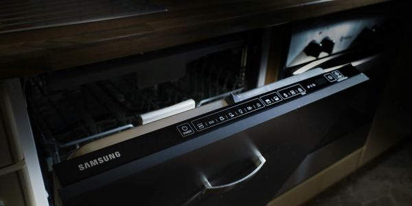 Samsung dishwasher with digital control panel partially opened under a kitchen counter.