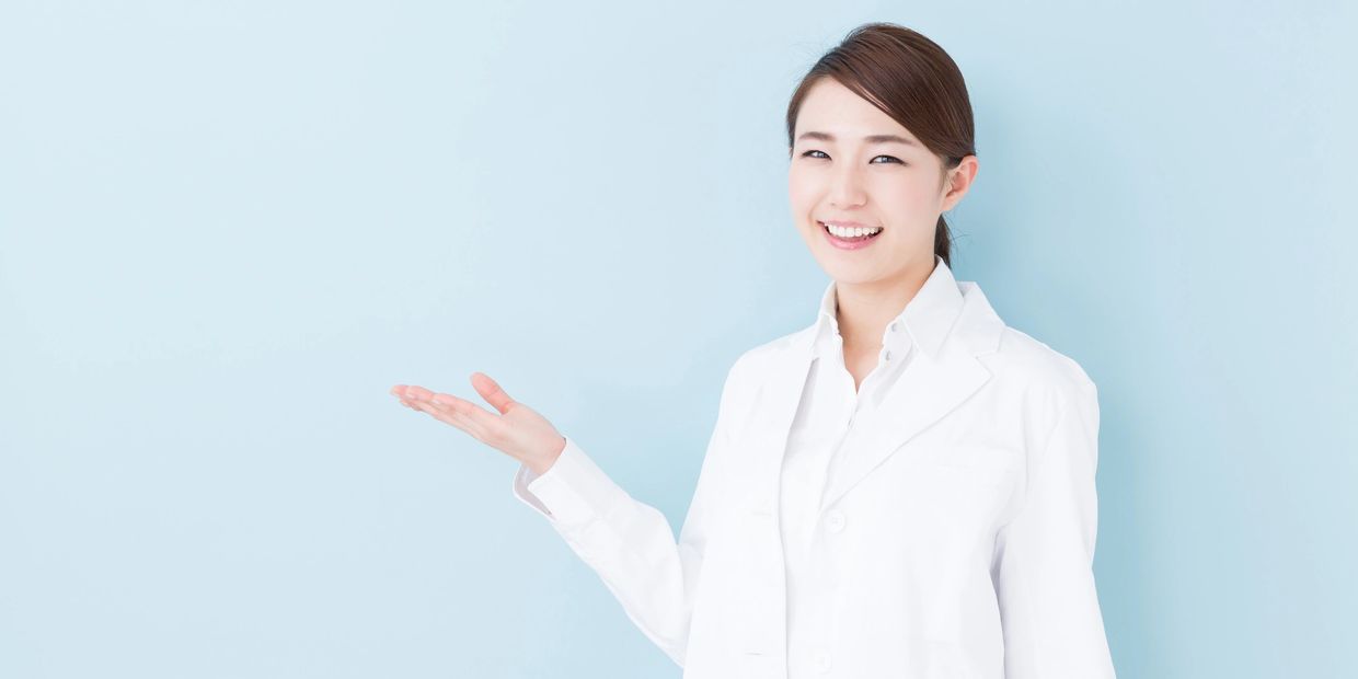 Smiling woman in white coat presenting with open hand against a light blue background.