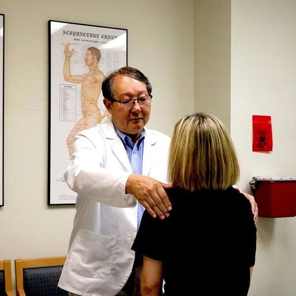 Dr Li assessing a patient in an acupuncture clinic treatment room with acupuncture chart.