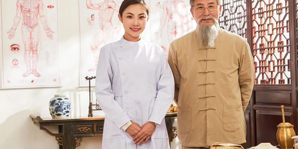 An older male and younger female Chinese Medicine Doctors in a clinic room looking at us.