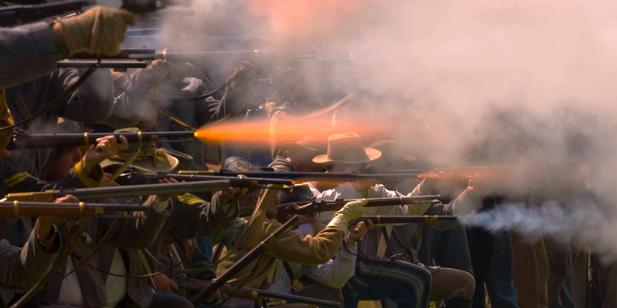 Group of men firing rifles in a smoky battlefield scene.