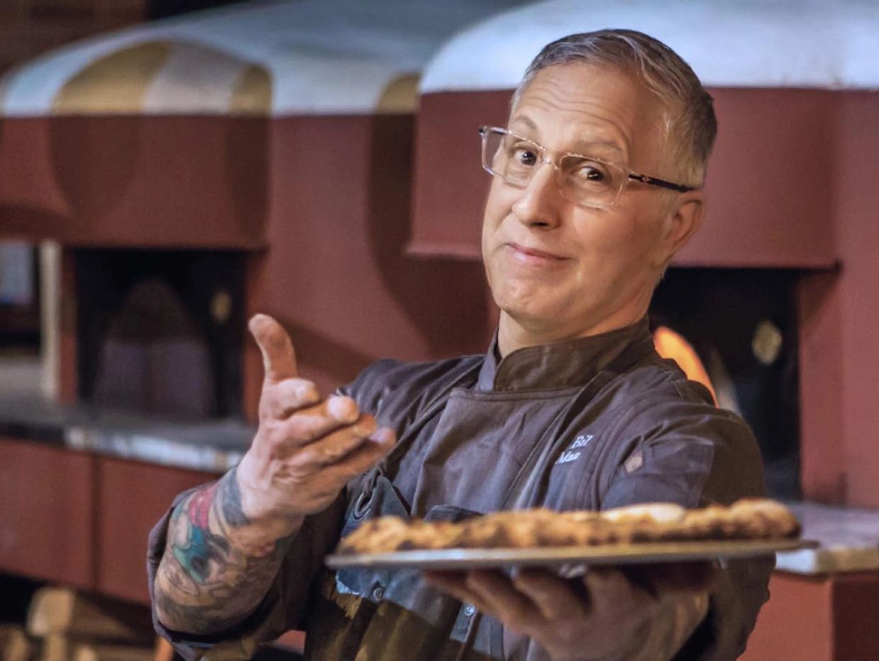 Chef presenting a freshly baked pizza with a confident smile.