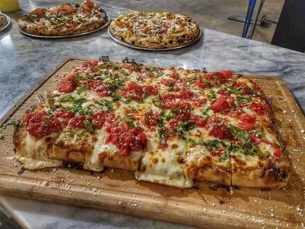 Rectangular pizza with melted cheese, tomatoes, and herbs on a wooden board.