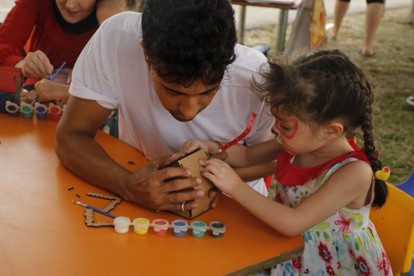 A man helps a young girl paint a wooden craft at a table.
