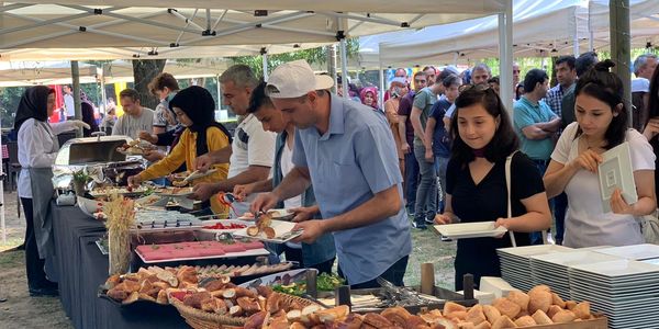 People serving themselves food at an outdoor buffet under tents.