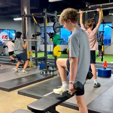 Teenagers working out with weights in a modern gym setting.