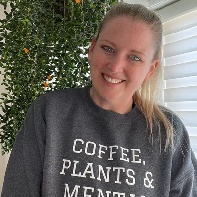 Allison wearing gray sweatshirt that reads Coffee, Plants & Mental Health 