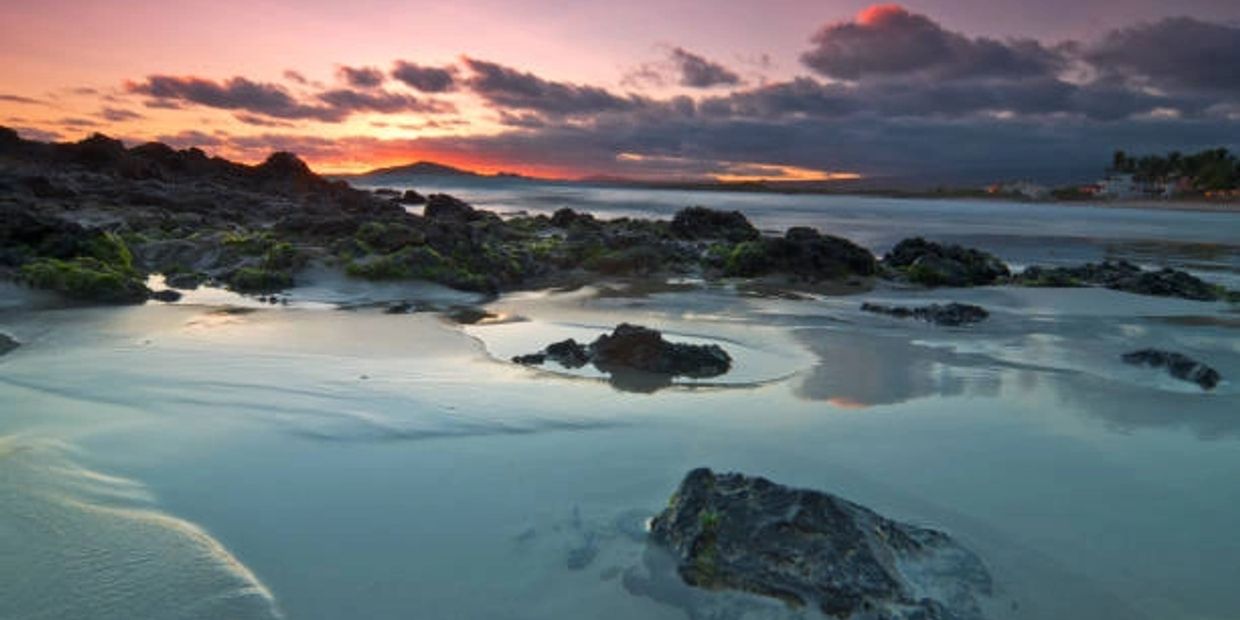 Sunset over a rocky beach with calm water and scattered clouds.
