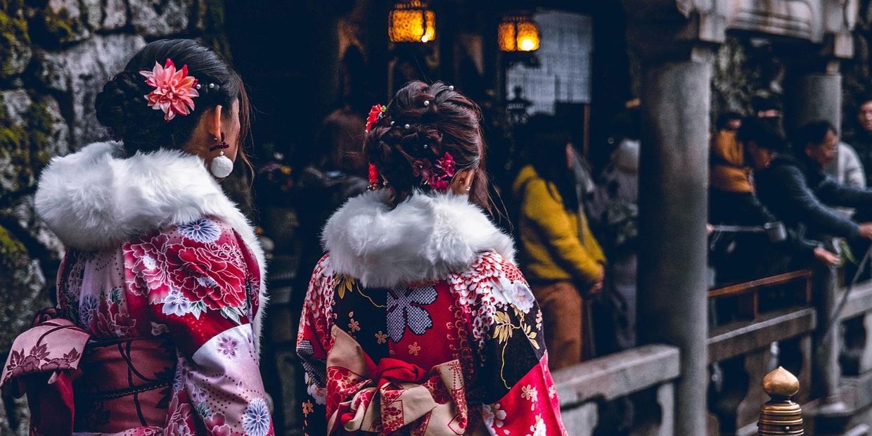 Two women in floral kimonos with fur collars and hair ornaments at a traditional event.