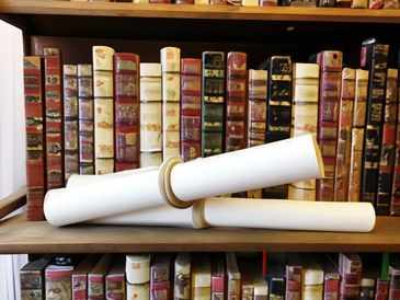 Two rolled white scrolls resting on a wooden shelf with vintage books behind.