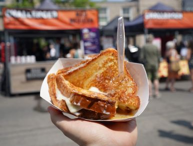 Hand holding a grilled cheese sandwich at an outdoor food market.