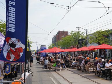 People enjoying an outdoor event with red umbrellas and Ontario's lumberjack banners.