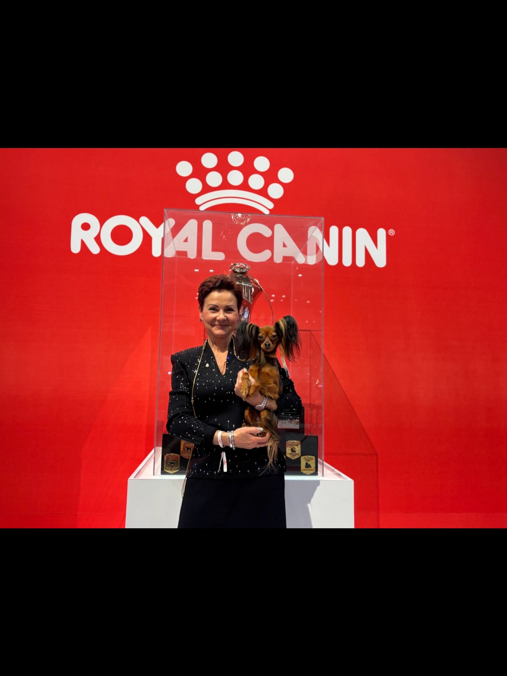 Woman holding a small dog in front of a Royal Canin backdrop.