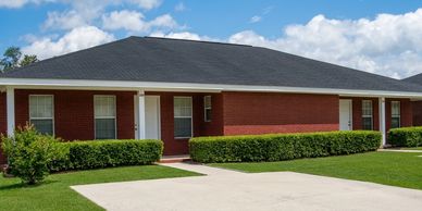 Red brick duplex with black roof and green hedges under a blue sky.