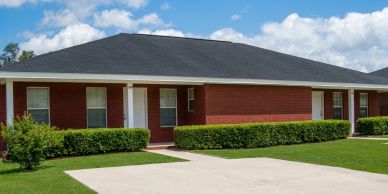 Red brick duplex with black roof and green hedges under a blue sky.