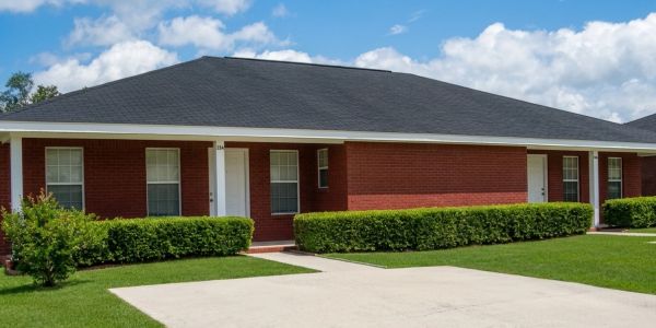 Red brick duplex with black roof and green hedges under a blue sky.
