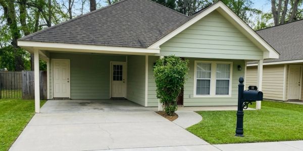 A single-story green house with a carport and a black mailbox.