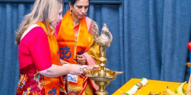 Two women lighting a traditional lamp during a cultural ceremony.