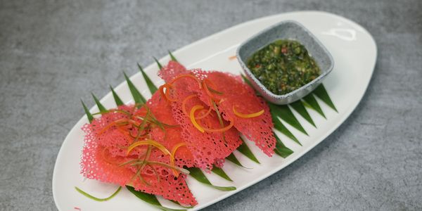 Red crispy snack with dipping sauce on a white plate.