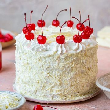 A white chocolate cake topped with whipped cream and cherries.