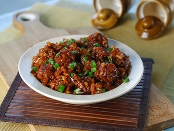 Plate of spicy and saucy meatballs garnished with chopped green onions.