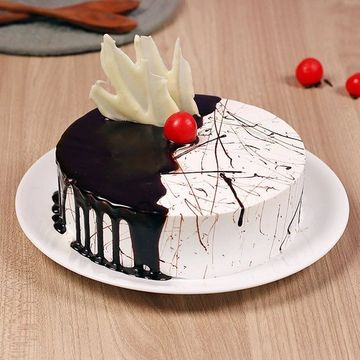 Elegant black and white cake with chocolate drizzle and a red cherry on top.
