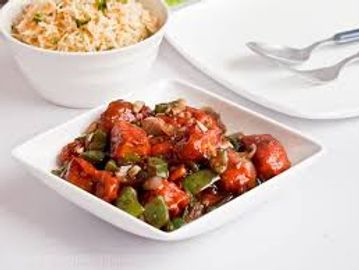 A bowl of spicy chicken curry with a side of rice on a white table.
