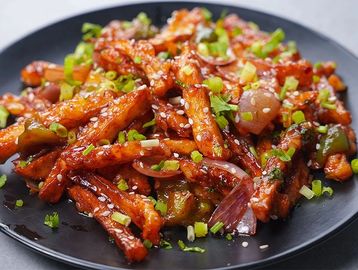 Spicy stir-fried potato fries with vegetables and sesame seeds on a black plate.