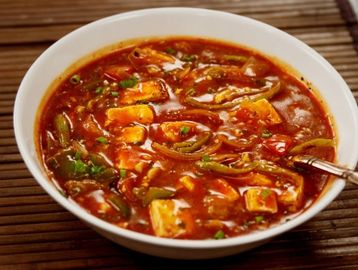 A bowl of spicy paneer curry with vegetables and herbs.