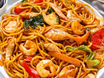 Plate of shrimp chow mein with vegetables and chicken.