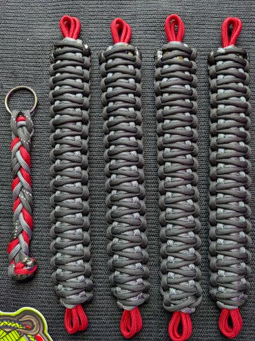 Five braided paracord keychains with red and gray colors on a dark surface.