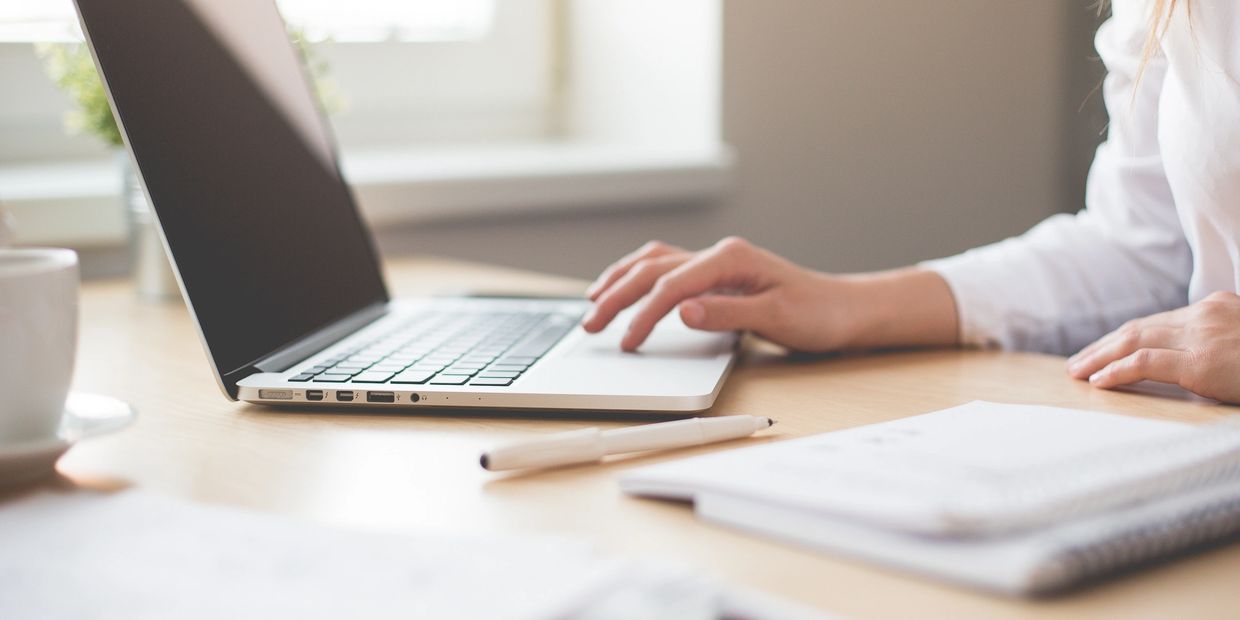 A laptop computer on a desk with someone's hands using the keyboard