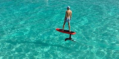 Person riding a hydrofoil board over clear turquoise water.